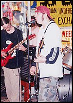 A band playing a MUM sidewalk jam around 2000, under the Meridian Underground skyline banner
