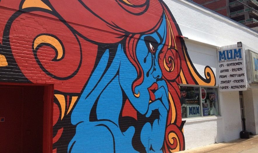 The MUM mural: a blue woman with flowing red hair and a tear in her eye, painted on the side of the store